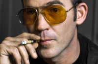 1977 portrait of Hunter S. Thompson smoking a cigarette wearing yellow tinted glasses